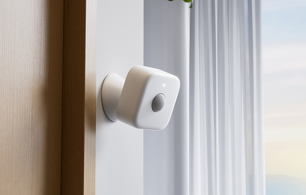 A white motion sensor on a movable mount by a window with a curtain.