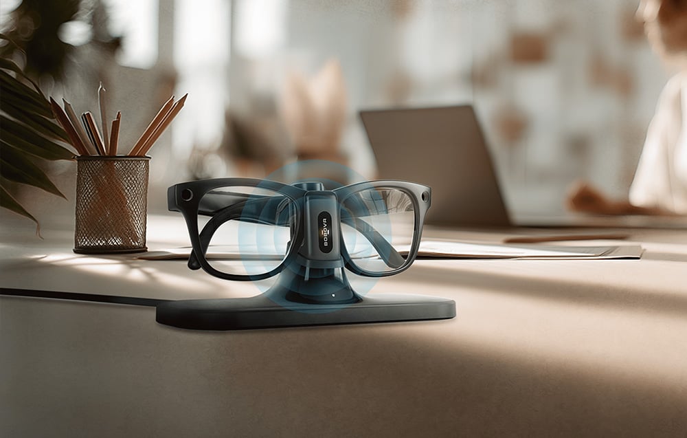 Smart glasses compatible with BOBOVR CG2 placed on a magnetic docking station on a desk in a modern workplace.
