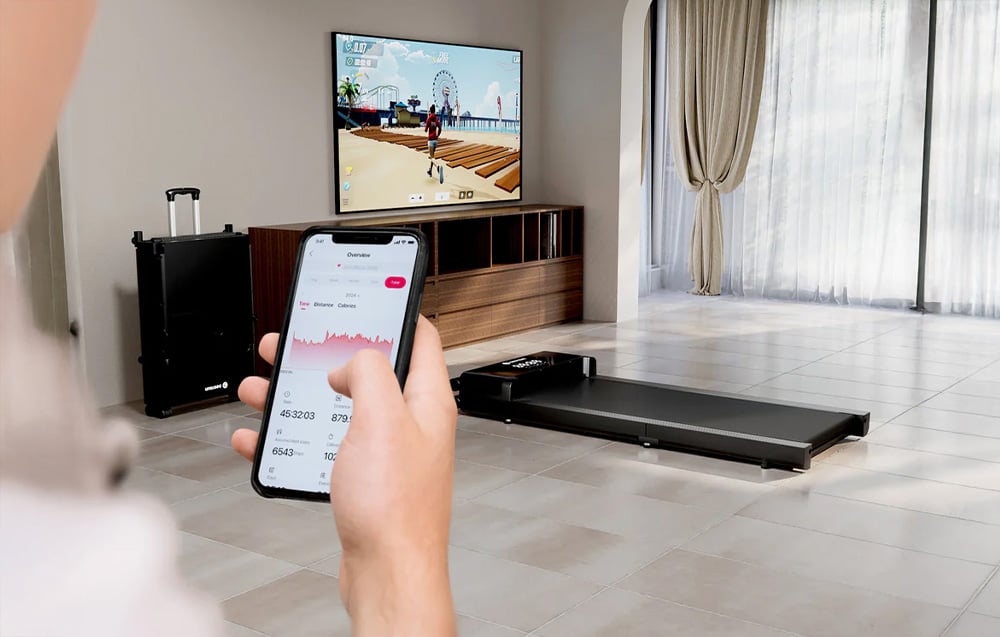Hands holding a smartphone with a fitness app against the background of a living room with a treadmill and TV