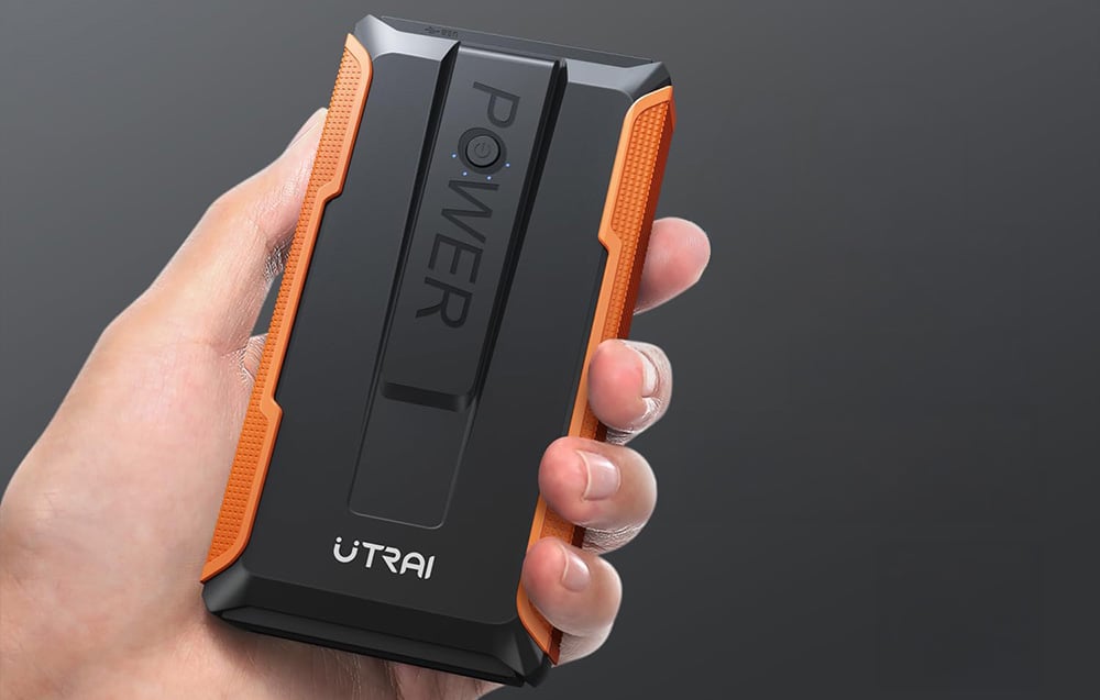 A handy car jump starter with a black-and-orange casing held in a person’s hand.