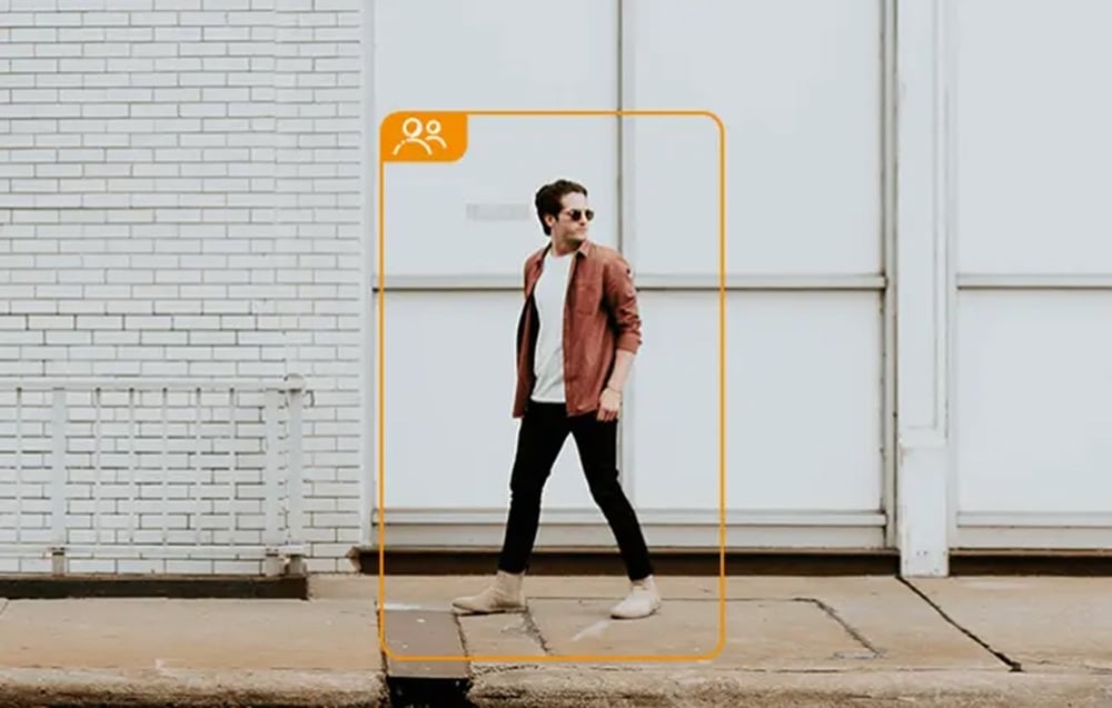A man wearing sunglasses walking on a sidewalk, framed in an orange border with an icon of two people