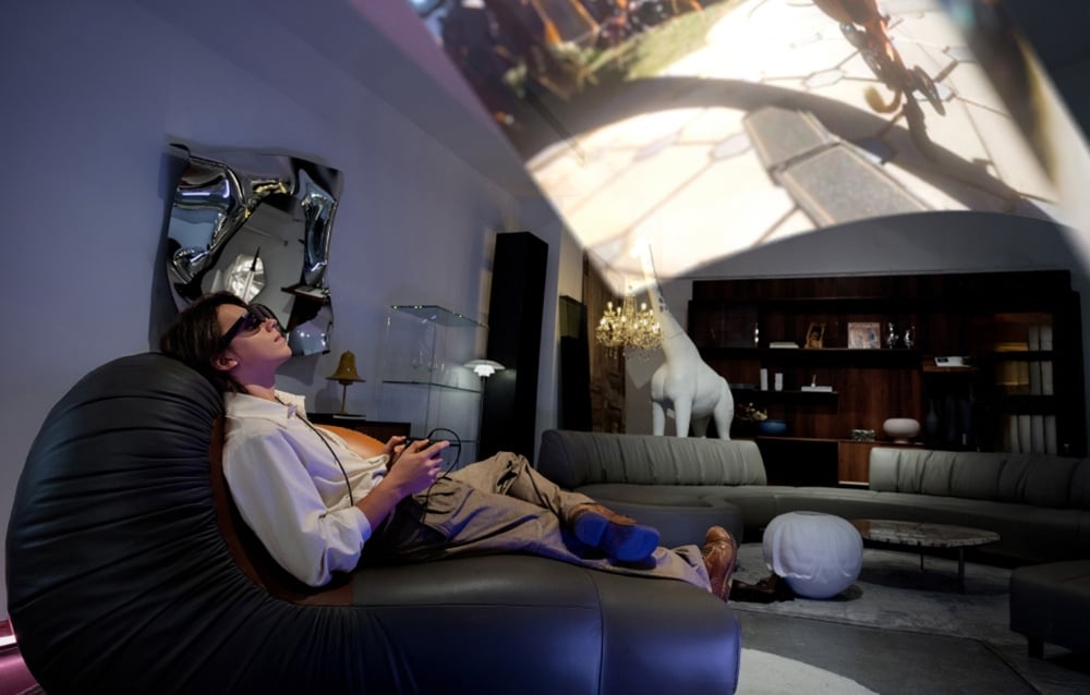 A man in a large living room playing a game on a screen with AR glasses