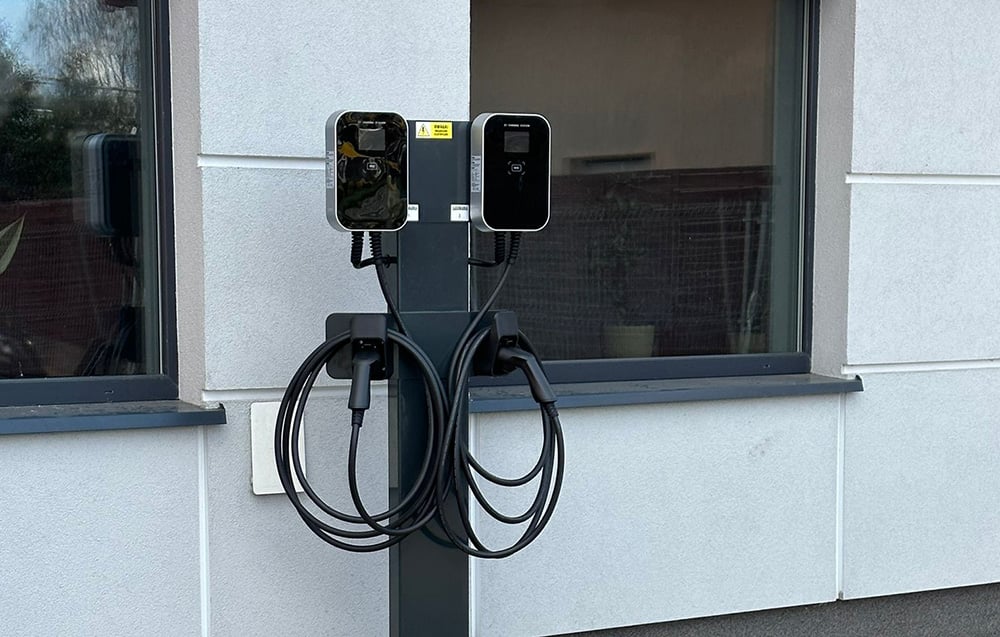 A dual electric vehicle charging station mounted on a freestanding post in front of the building.