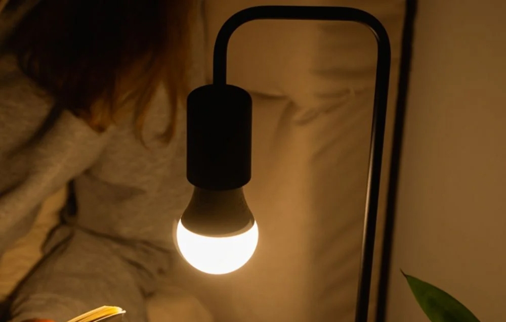 A close-up of a black, bent desk lamp with a warm light bulb on in a dark room