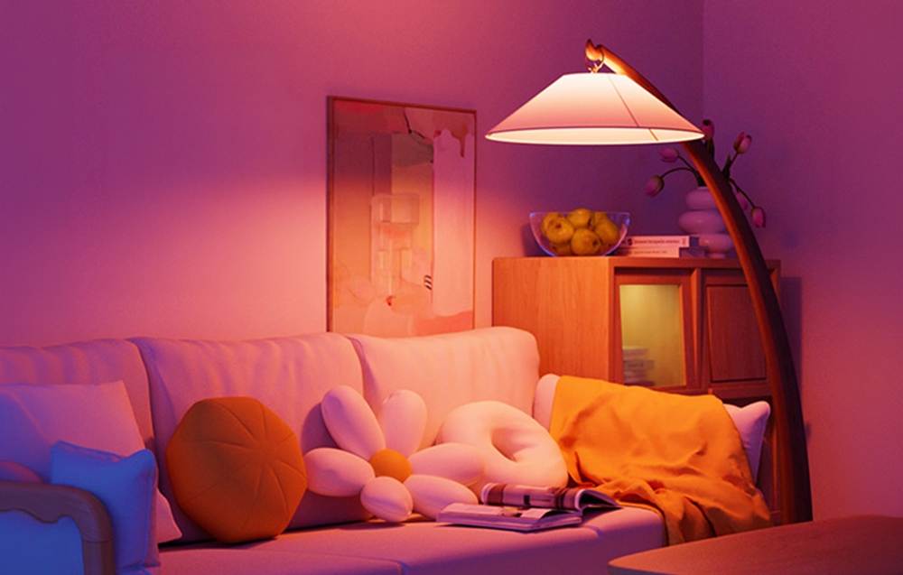 A living room with a sofa and flower-shaped pillows, illuminated by the purple-pink light of a standing floor lamp.