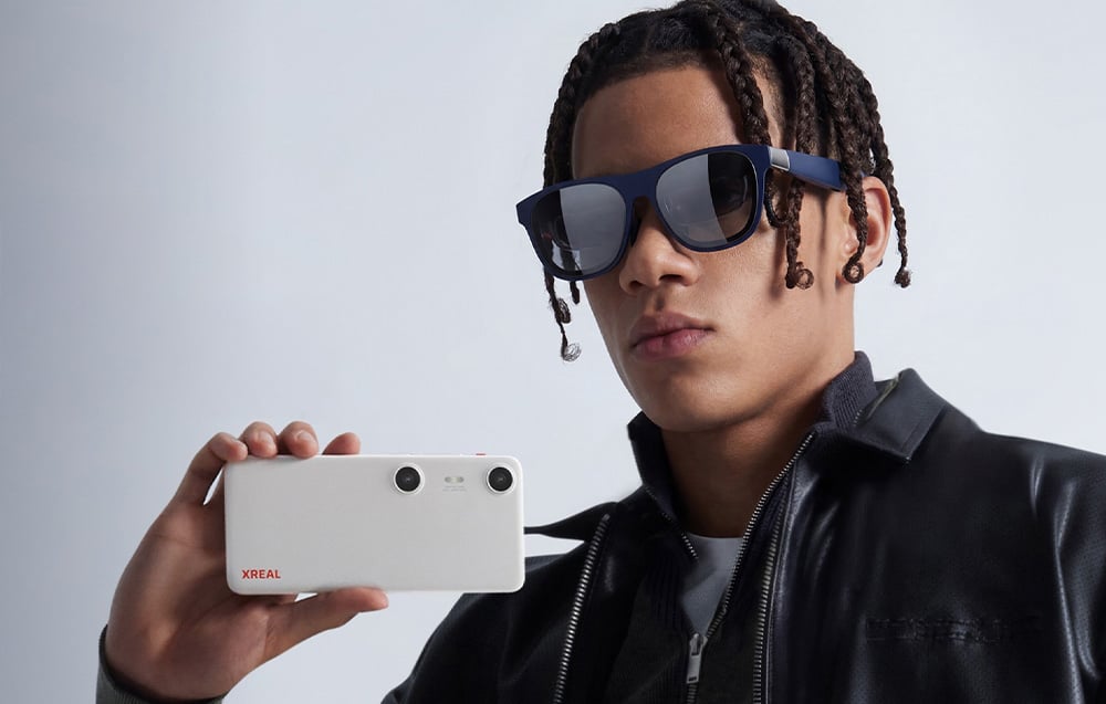 A man with dreadlocks and AR glasses holds an adapter in his hand