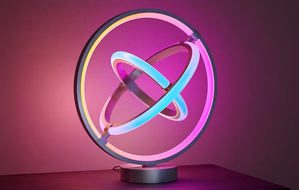 A desk lamp consisting of three glowing neon circles, placed on a dark tabletop.