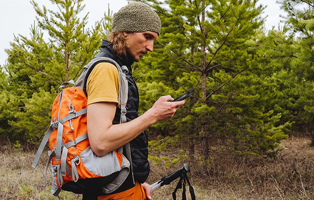 Man wearing a backpack holding a smartphone while standing in a forest