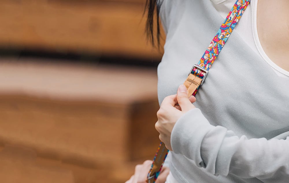A woman in a light-colored T-shirt adjusts the length of the PGYTECH strap, which is slung over her shoulder