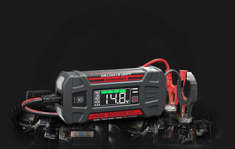A jump starter connected by cables to a car battery, displaying the voltage on the screen.