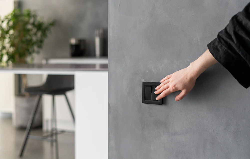 A hand pressing a black wall switch mounted in a gray concrete wall in a modern interior
