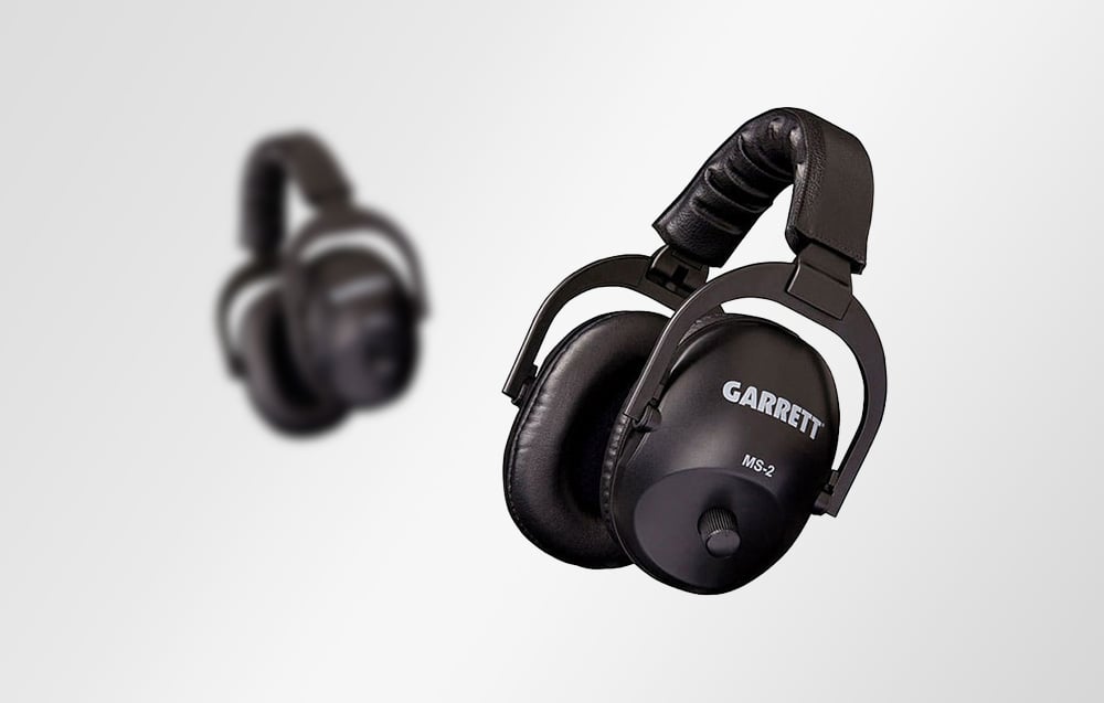 Two pairs of black metal detector headphones, one model is smeared in the background