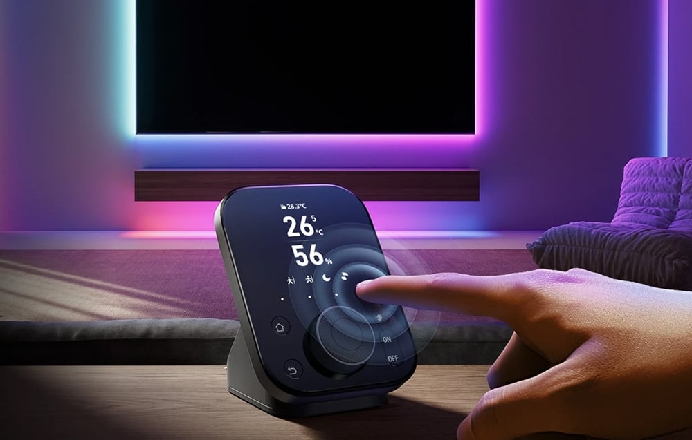Hand operating the SwitchBot remote control in front of the TV with color LED backlighting in the living room