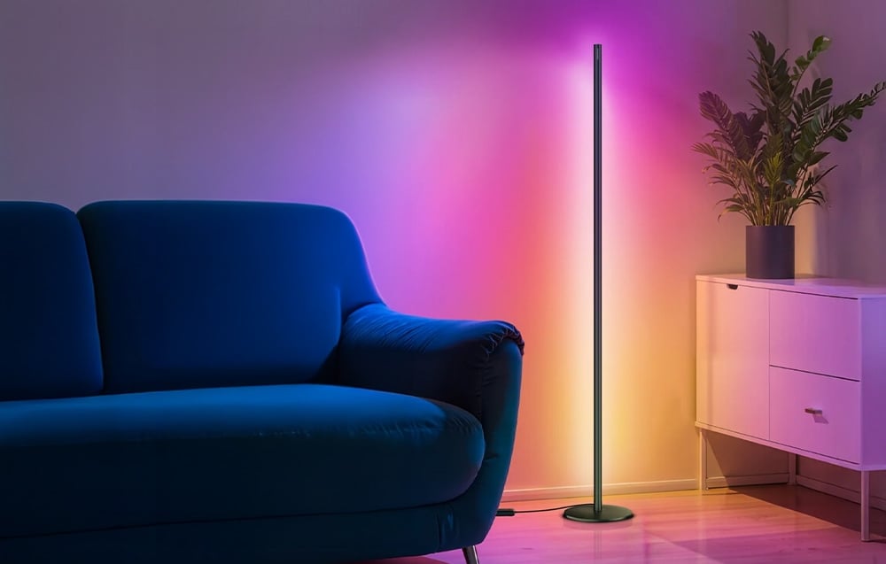 A slender floor lamp illuminating a corner of the living room with a blue sofa in shades of purple and pink.