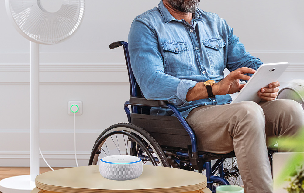 A man in a wheelchair operating a tablet, in the background a fan connected to a smart outlet with green illumination