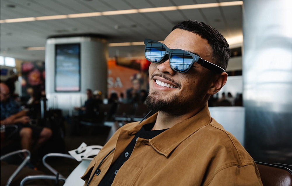 Man in sunglasses smiles while sitting in airport waiting room