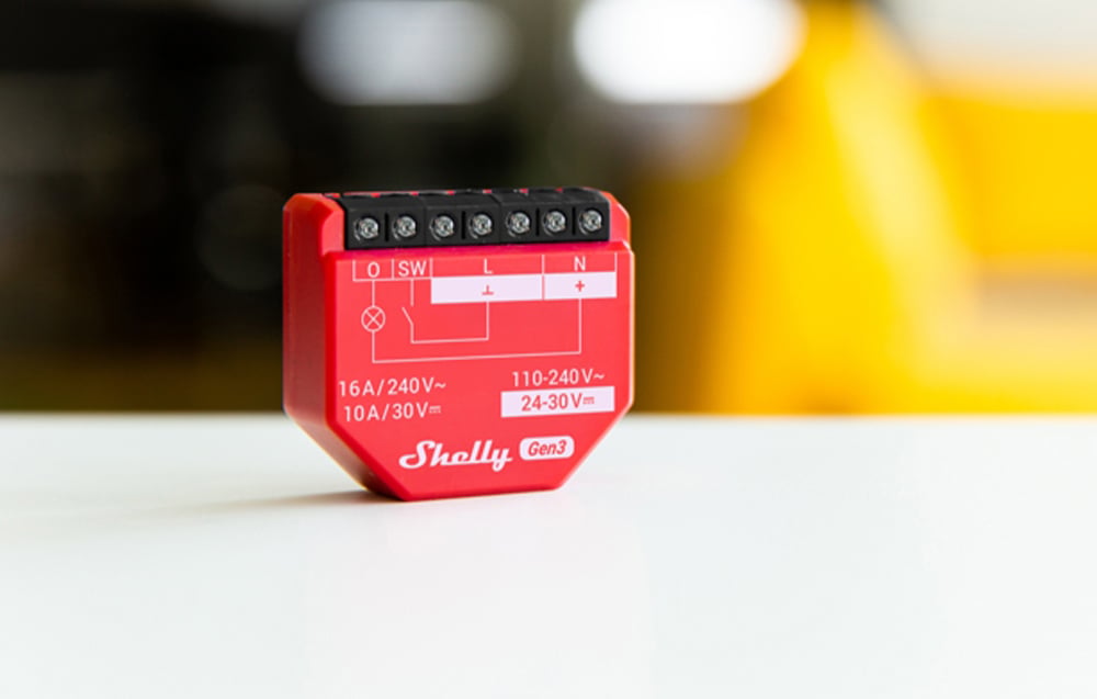 Red Shelly 1PM Gen3 module stands on a white surface, with technical markings and connectors visible from the front