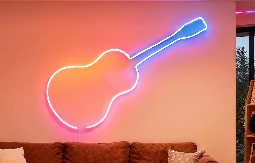 A glowing neon sign shaped like a classical guitar on a light-colored wall above a brown sofa.