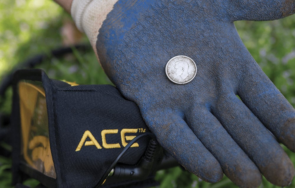 A gloved hand holding the coin next to the metal detector.