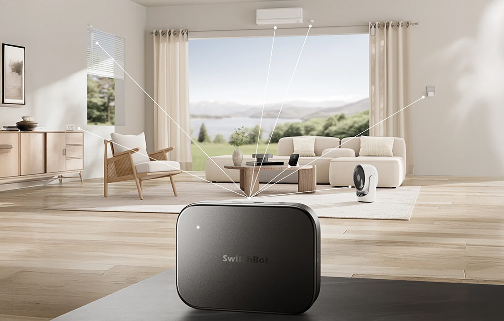 The SwitchBot Gateway placed on a table in a modern living room, connected to various smart home devices in the background.