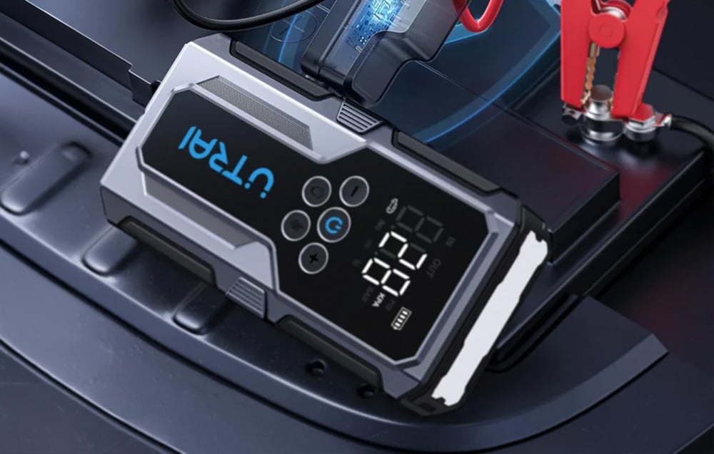 A car jump starter connected with a red clamp to a battery under the vehicle’s open hood.