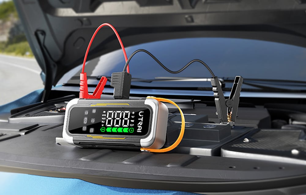 A car starter connected by cables to a battery under the open hood of a car.