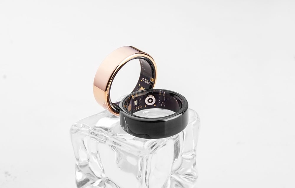 Two smart rings—gold and black—on a crystal platform against a white background
