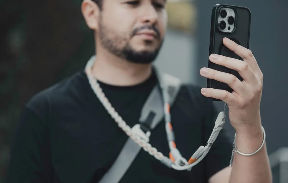 A man in a black T-shirt uses a smartphone mounted to a PGYTECH neck strap