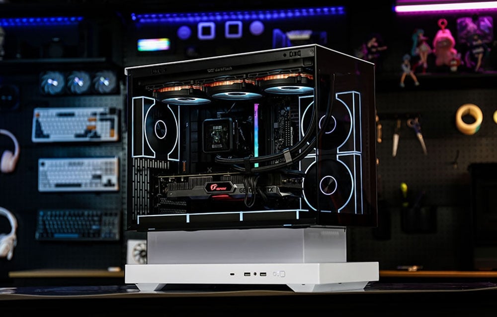 Transparent computer case with white base against a dark workshop with keyboards and tools