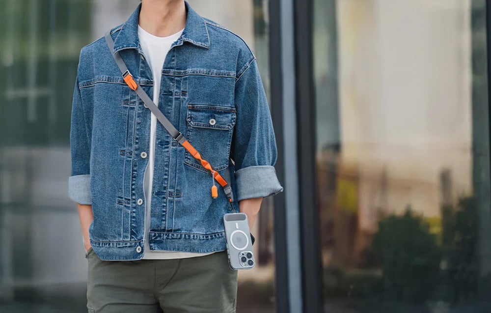 A man wearing a denim jacket and a PGYTECH neck strap, to which a smartphone is mounted