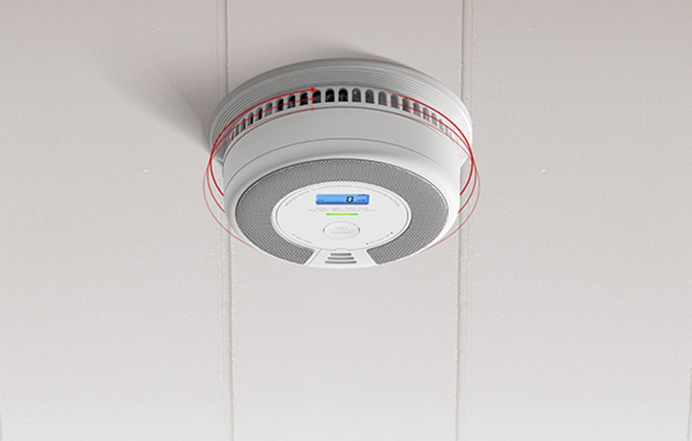 A carbon monoxide detector mounted on the ceiling with red arrows indicating airflow through the side vents