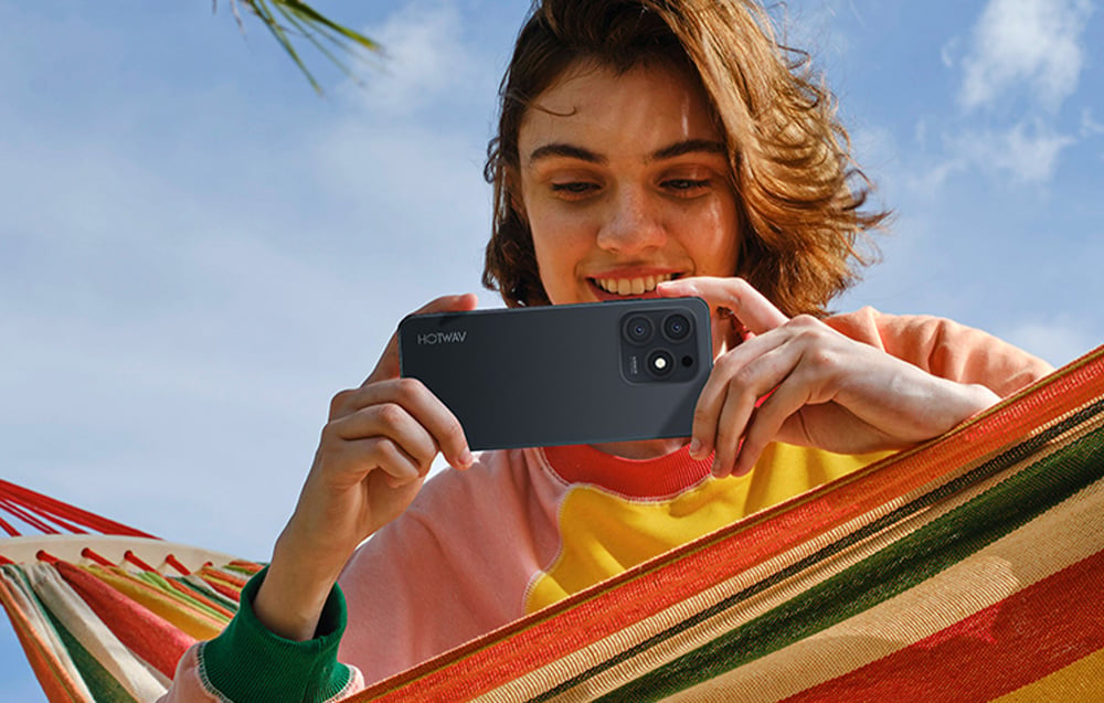 A woman lying in a hammock taking a photo with a Hotwav smartphone