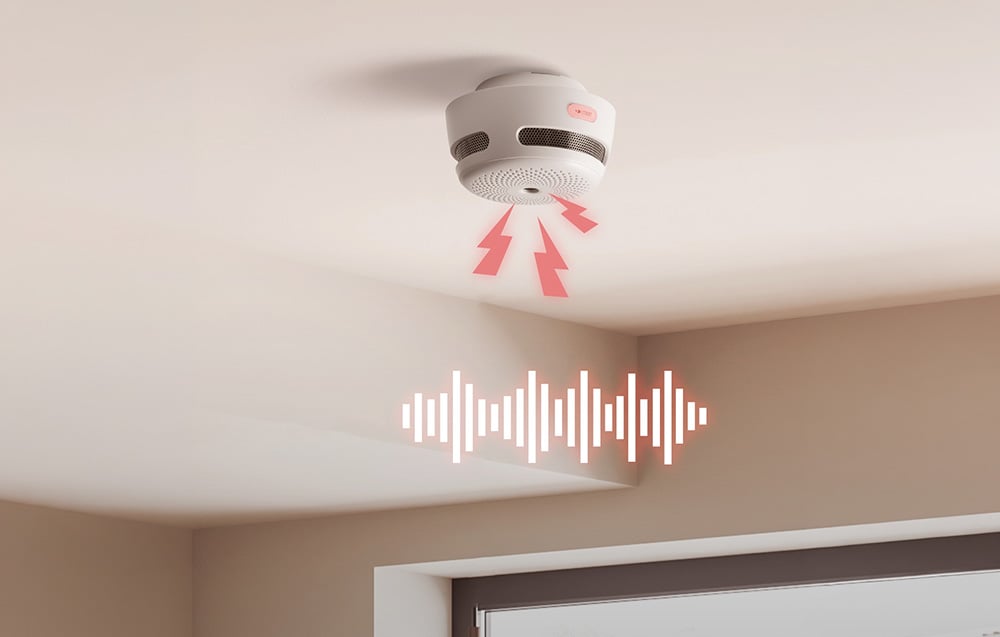 A round smoke detector mounted on the ceiling with red flashing lights and a graphic sound wave below