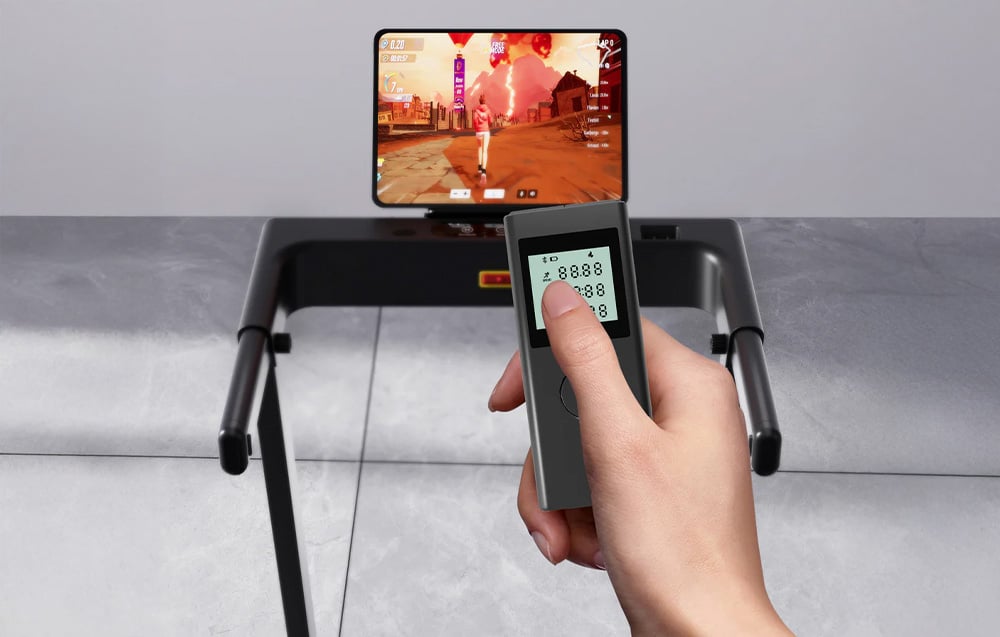 Top view of the treadmill panel with a screen and a hand holding a remote control with a display