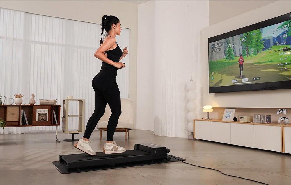 Woman in black outfit running on a flat treadmill during a virtual workout displayed on a TV