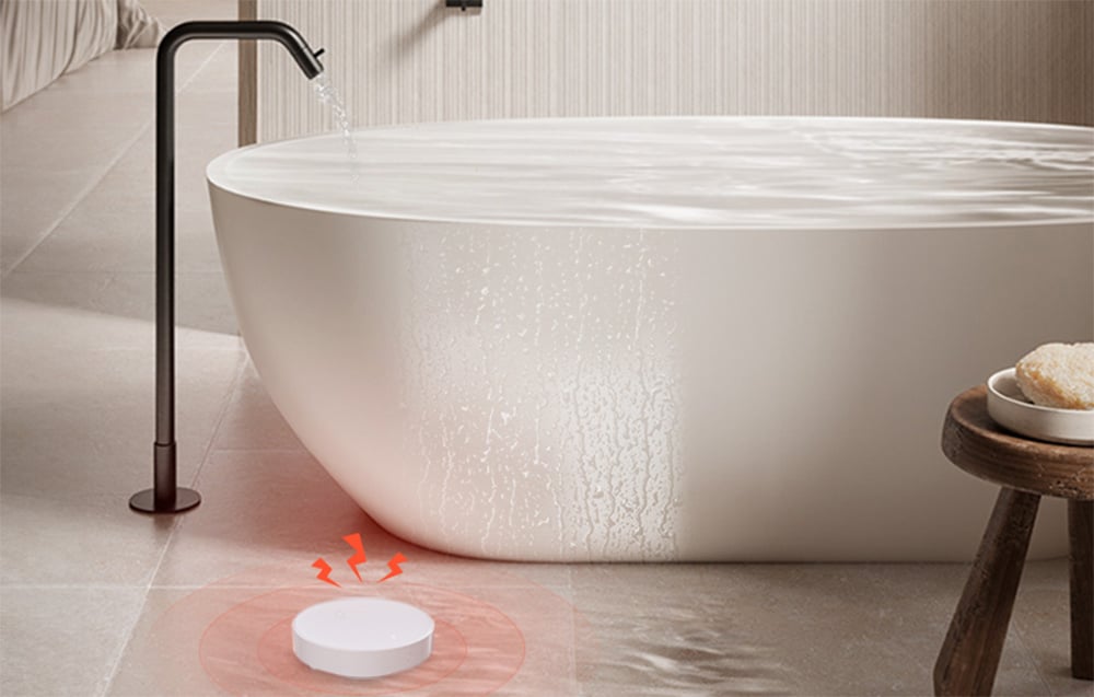 Round flooding sensor with red light indicator placed on the floor next to the overflowing bathtub
