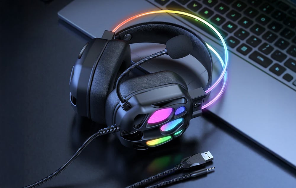 Black over-ear headphones with illumination lie on a table next to a laptop and cable