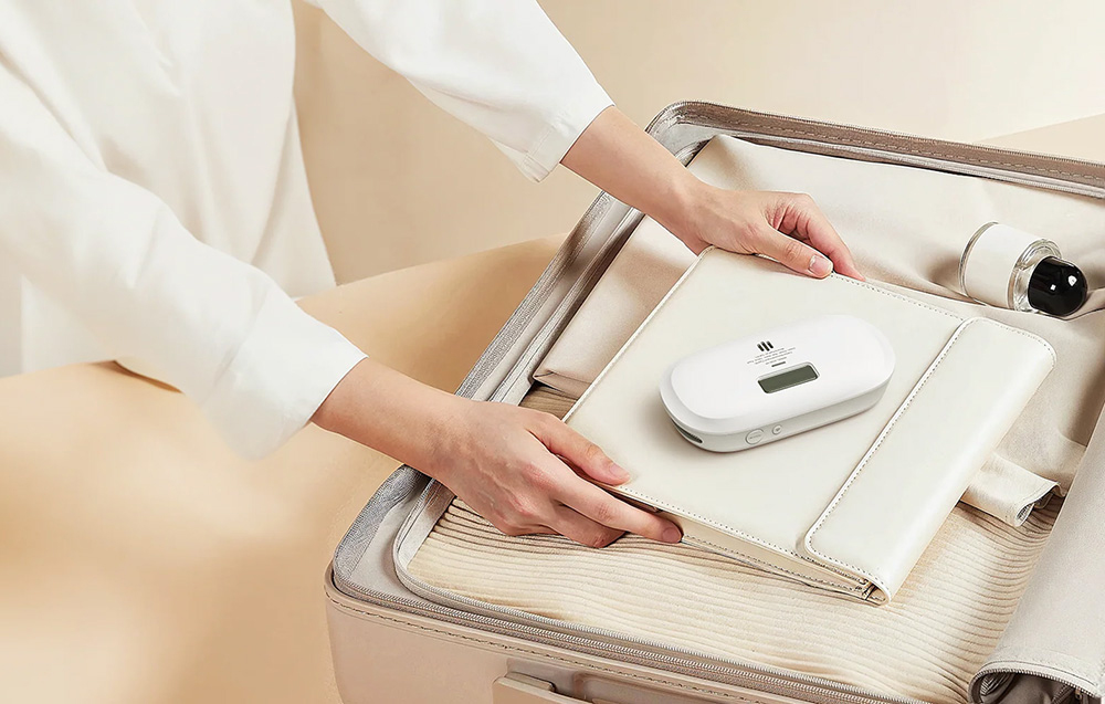 A person packing an X-Sense carbon monoxide detector into a suitcase