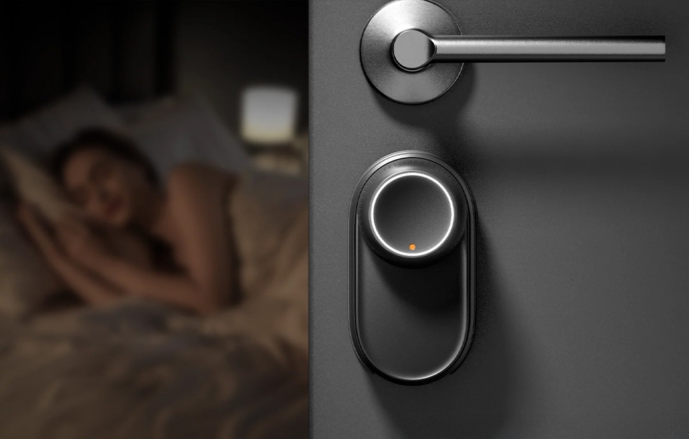 SwitchBot lock with white LED backlight mounted on dark bedroom door, person sleeping in background