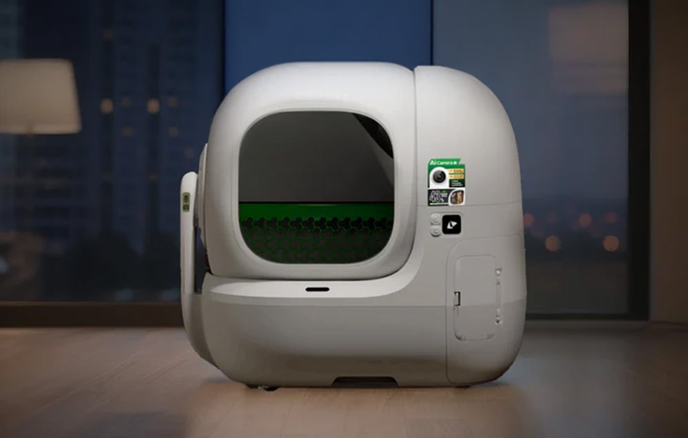 White automatic cat litter box with AI camera and green strainer, standing in a modern living room