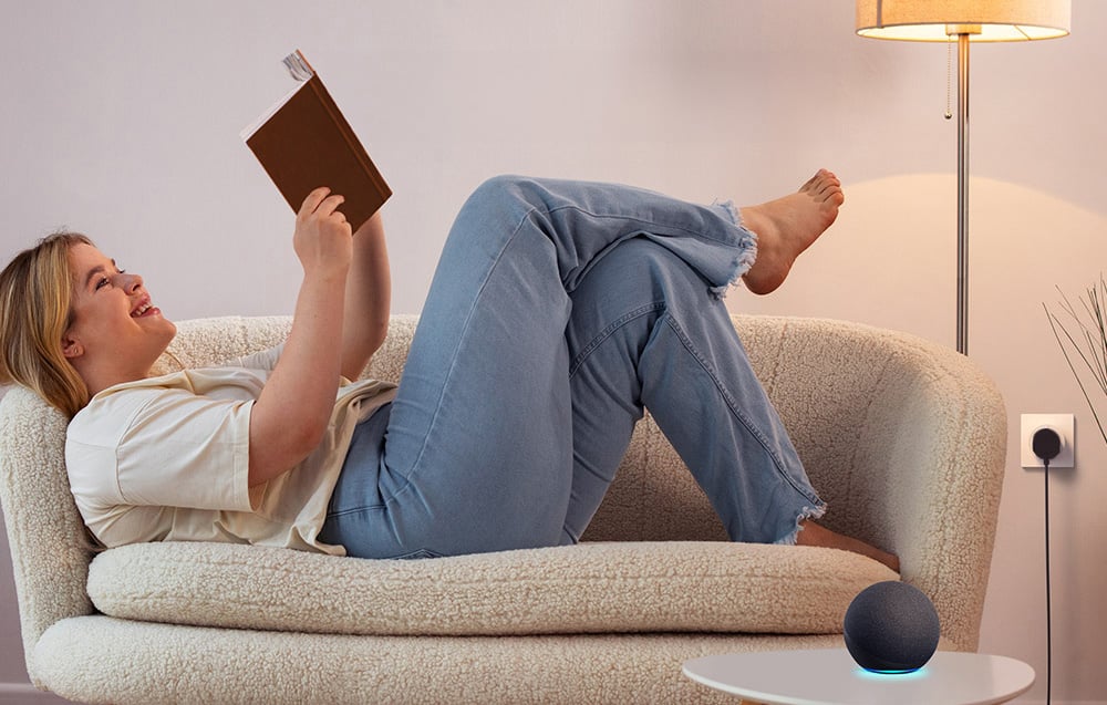 Woman reading on the sofa next to the lamp and voice assistant speaker