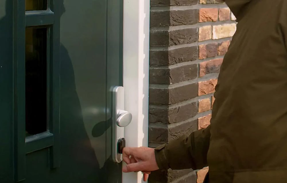 White smart lock on green door - hand inserts key into lock cylinder