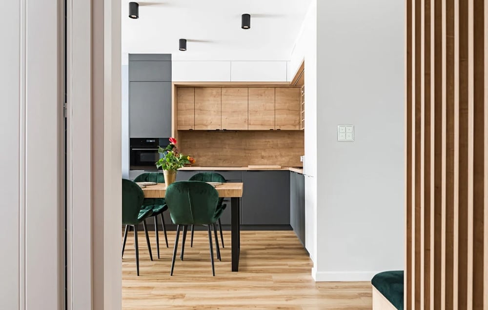 A bright kitchen with a wooden table, green chairs, and a wall switch