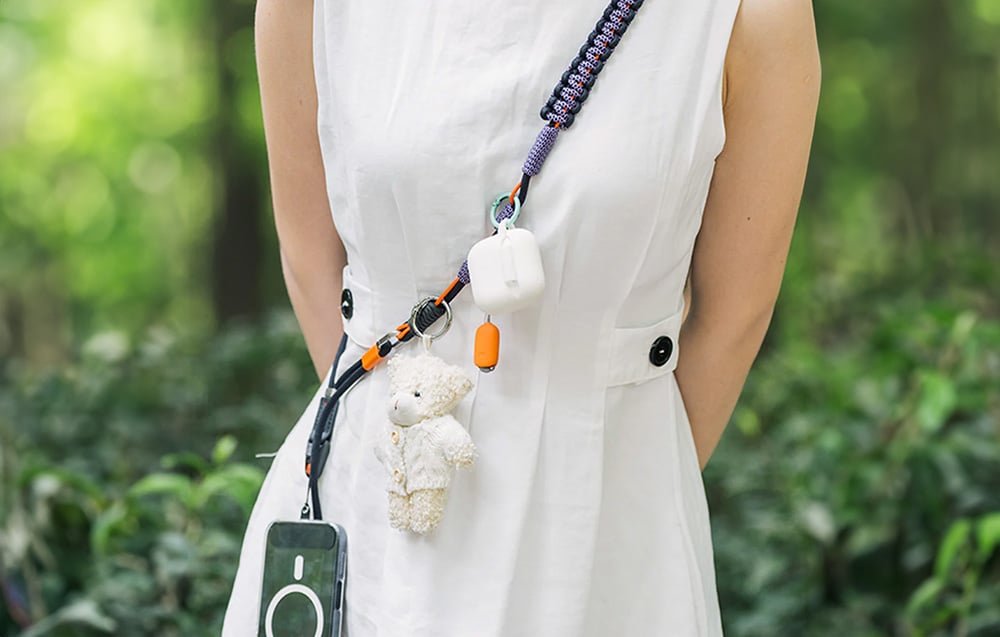 A woman in a white dress wears a black PGYTECH strap to which a smartphone and accessories are mounted