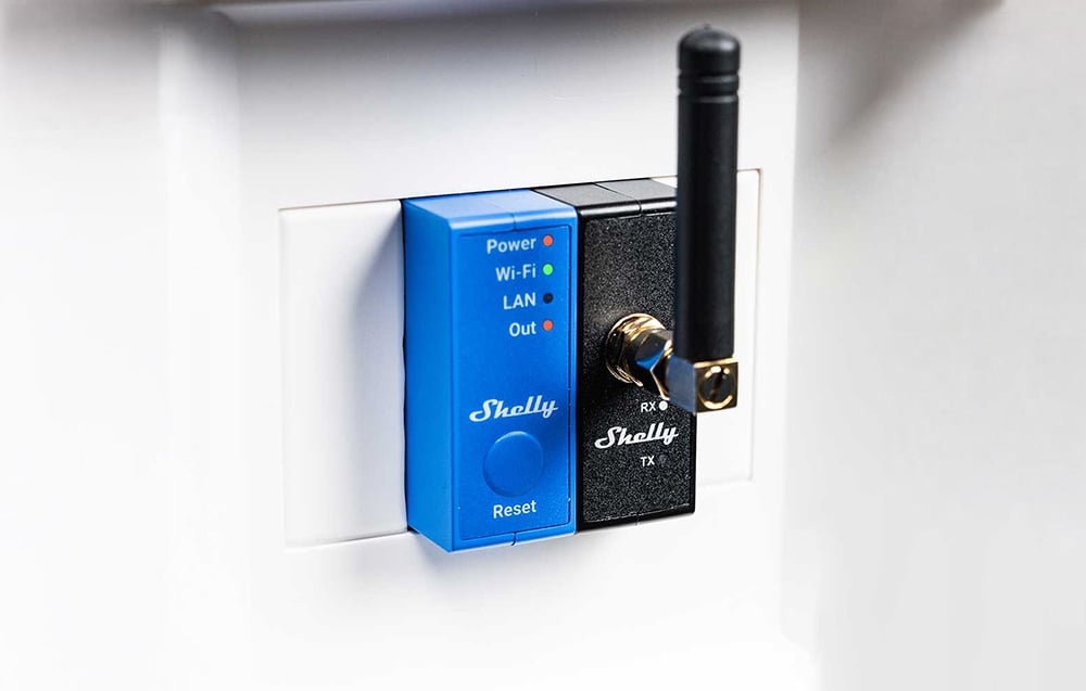 A blue and black module with the word “Shelly” and an antenna connected to a white wall outlet