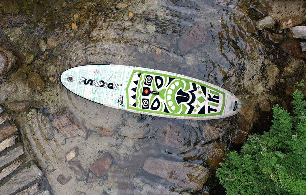 A colorful Funwater surfboard is lying on the water, surrounded by rocks and plants