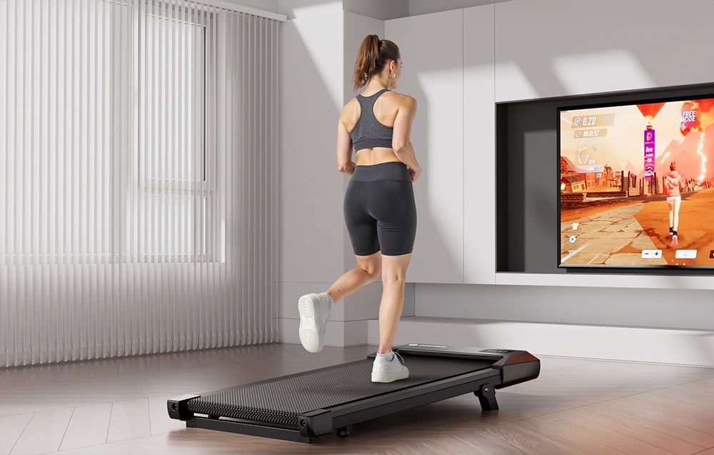 A woman runs on a flat treadmill while training with an interactive app displayed on a TV