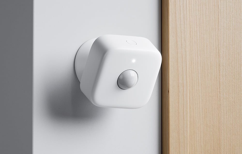 Presence sensor mounted on a white wall next to a wooden door frame.