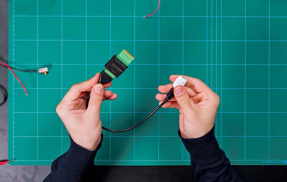 Hands holding a black wire connected on one end to the ADDON SSR module and on the other to a white plug