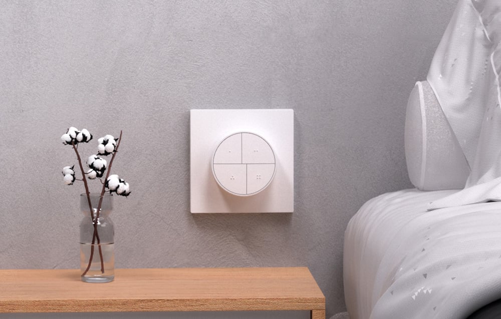 Smart button on the wall above the bedside table with a vase of cotton flowers, next to a bed with bright bedding